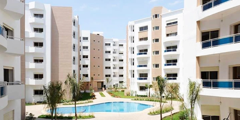 marché de l'immobilier - Résidence moderne avec immeubles blancs et beiges entourant une piscine commune, espaces verts et palmiers.