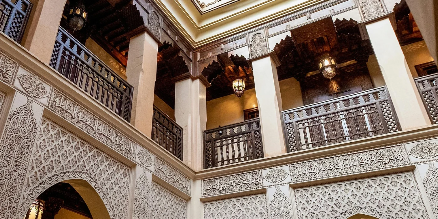 Immobilier à Agadir - Intérieur d’un riad traditionnel marocain avec balustrades en bois sculpté, plafonds en bois travaillé et décorations murales en stuc ciselé.