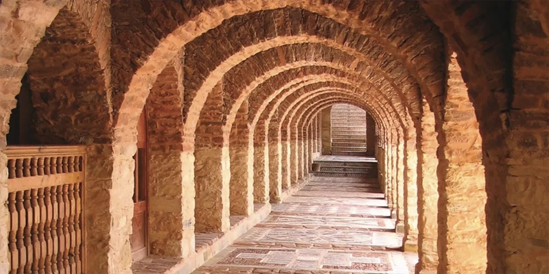Galerie voûtée en pierre de la Médina Polizzi à Agadir, avec arches successives et sol pavé dans un style architectural traditionnel marocain.