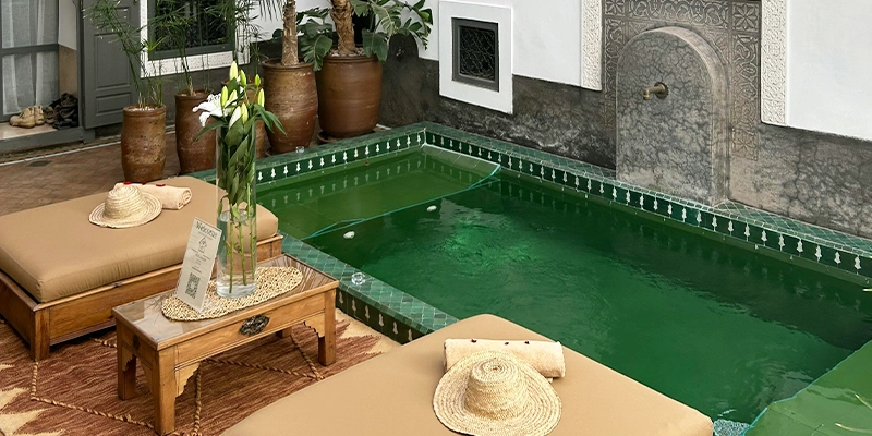 Petit bassin décoratif dans un riad marocain, avec fontaine murale sculptée, lits de repos et ambiance intimiste.
