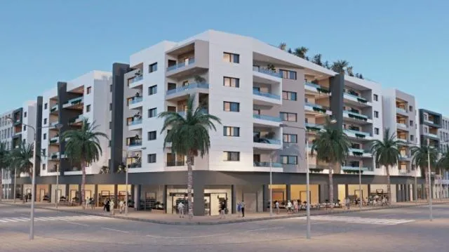 Immeuble appartement résidentiel moderne à Agadir avec façades contemporaines, balcons spacieux, palmiers en bord de rue et commerces au rez-de-chaussée.